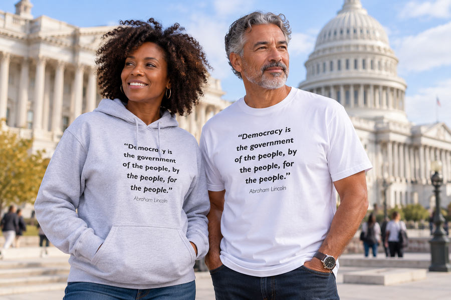 Woman in a gray hoodie and man in a white t-shirt, both printed with Abraham Lincoln’s quote "Democracy is the government of the people, by the people, for the people," standing in front of the U.S. Capitol