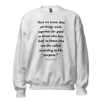 Unisex black sweatshirt with Romans 8:28 Bible verse printed in black text on front