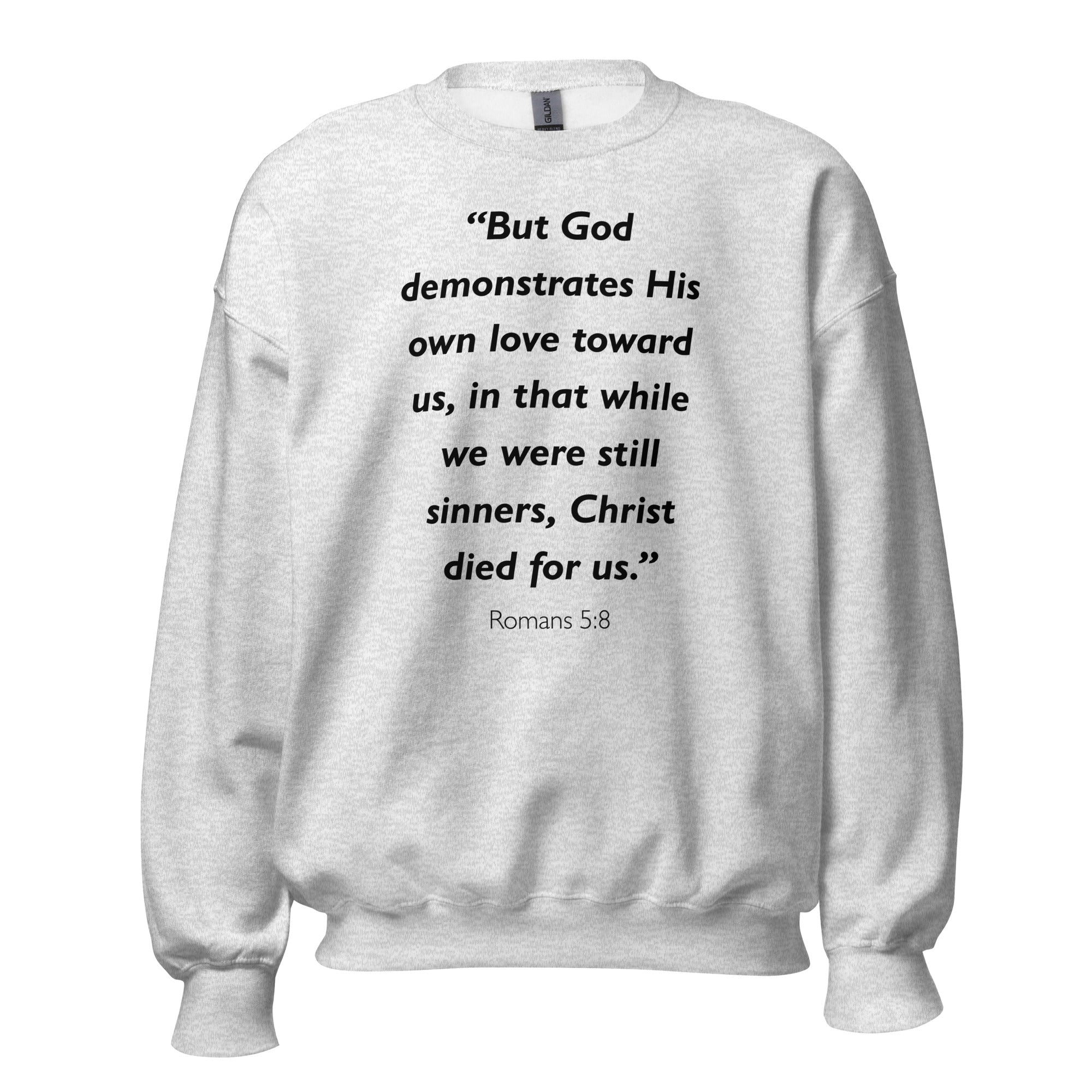Unisex heather gray sweatshirt with Romans 5:8 Bible verse printed in black text on front