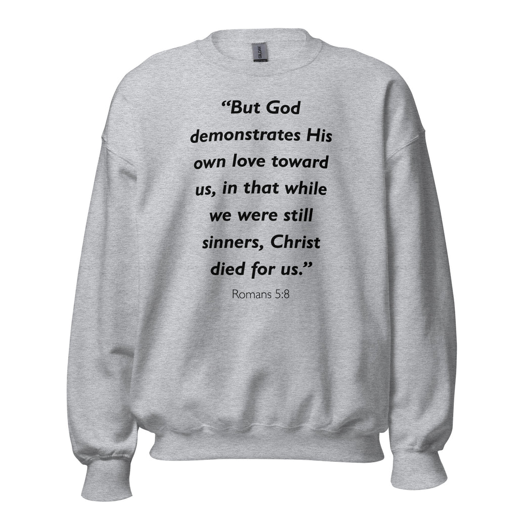 Unisex black sweatshirt with Romans 5:8 Bible verse printed in black text on front