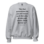 Unisex black sweatshirt with Romans 5:8 Bible verse printed in black text on front